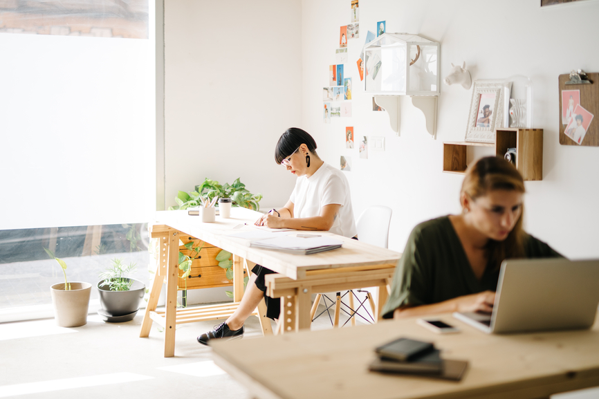 Trendy women sitting at wooden desks in contemporary stylish studio